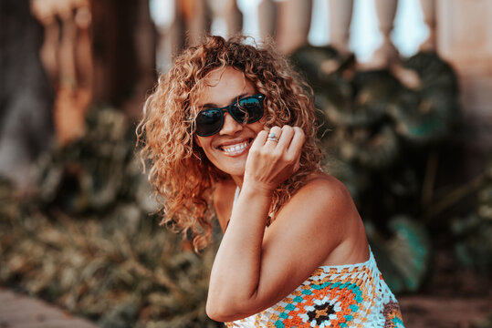 Smiling woman with curly hair wearing sunglasses and a colorful crochet top outdoors