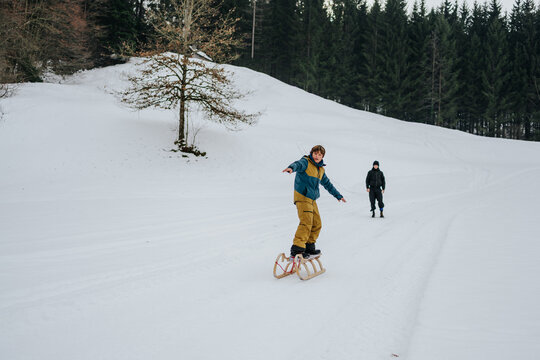 boy trying to surf a sled on snowy hillside
