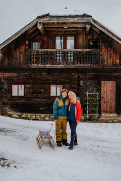 grandmother and grandson with sled standing in front of wooden c