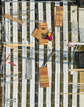 Aerial view of building construction and formwork with a worker in a red shirt and yellow hard hat on scaffolding in New Taipei, Taiwan.