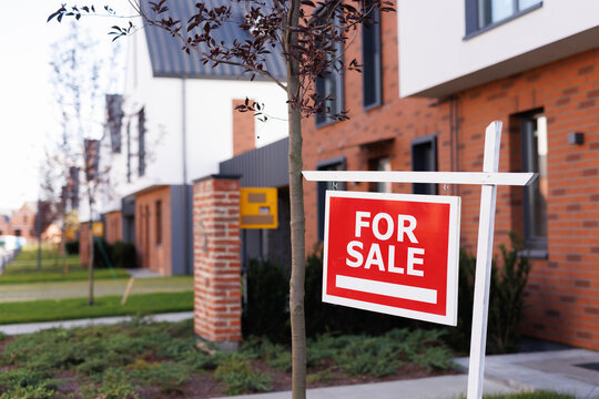 Focus on For sale sign in yard in front of blurred townhouse complex