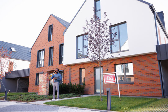 Serious black male realtor talking on cellphone in yard of townhouse