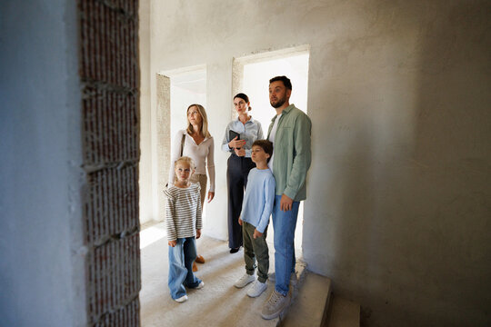 Adult female realtor showing new house inside to young focused family