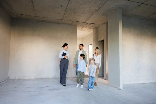Smiling adult female realtor showing new house inside to young family
