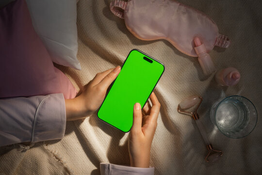Overhead view of hands holding a green screen smartphone on bed