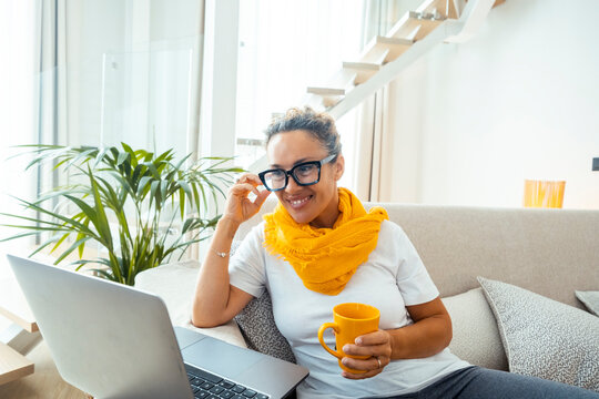 Smiling woman working on laptop at home with yellow scarf and coffee mug, remote work comfort