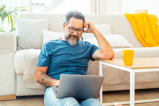 Middle-aged man working on laptop at home sofa, relaxed remote work and casual lifestyle scene