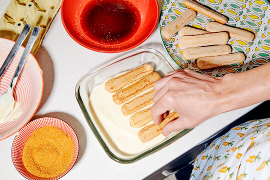a man places a new layer of ladyfingers on tiramisu