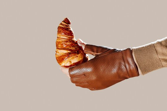a croissant is held by a man wearing leather gloves