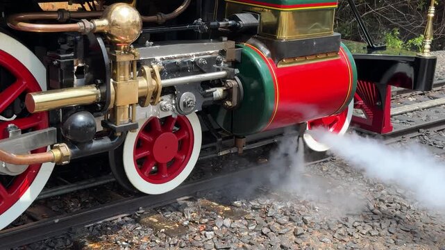 A close-up shows the wheels and mechanical parts of a vintage steam locomotive. The image highlights railway engineering and historic transportation technology.