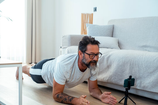 Middle-aged man doing a forearm plank at home while following a fitness video on smartphone