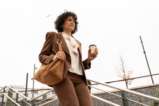Woman Walking Down Stairs While Holding a Coffee Cup in Hand