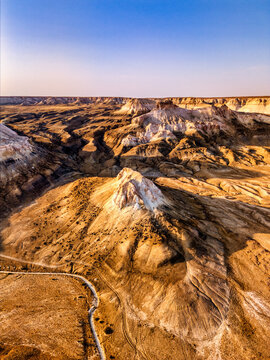 Aerial view of Bozhira landmark featuring white limestone cliffs and a winding dirt road across the vast desert landscape under a clear sky in Karakiya District, Mangystau Region, Kazakhstan.