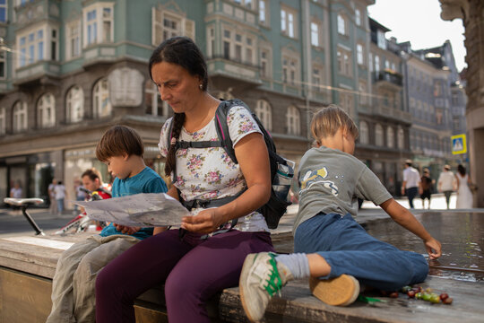 Mother and Children Explore City While Sitting by Water Fountain
