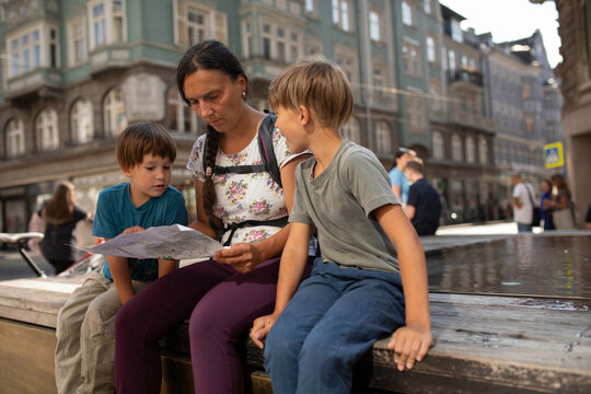 Two Children and their mother Learn From a Map in a City Square
