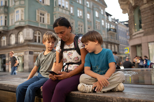 Mother and Children Sitting in a City Square Looking at Phone