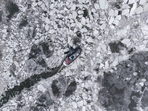 Tugboat navigating icy river with visible trail
