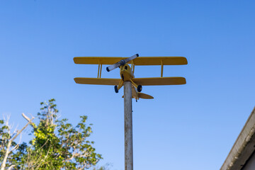 A yellow biplane decoration stands tall against a clear blue sky in a rural setting. Kawhia, Waikato, New Zealand. © Zenstratus