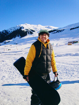 Man Carrying Snowboard Across Snowy Ski Area