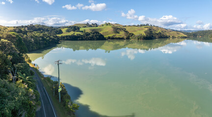 Aerial view of the verdant, rolling hills and a tranquil harbour in Kawhia Harbour, Owhiro, Waikato, New Zealand. The landscape showcases lush green pastures and dense forests. © Zenstratus