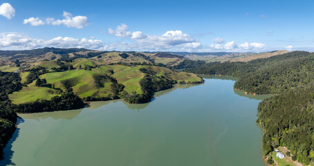 Aerial view of the verdant, rolling hills and a tranquil harbour in Kawhia Harbour, Owhiro, Waikato, New Zealand. The landscape showcases lush green pastures and dense forests. © Zenstratus