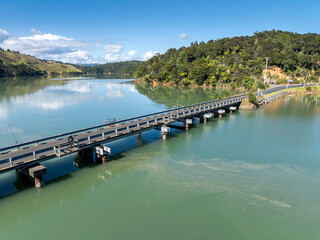 Fototapeta premium An aerial view of the scenic landscape of Kawhia Harbour, Owhiro, Waikato, New Zealand, featuring rolling green hills, a tranquil lake, and a bridge crossing the water.