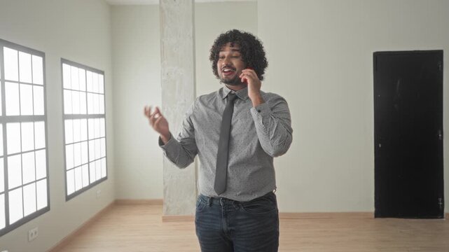 Man on smartphone holding phone to ear and gesturing with hand inside an empty building room; confident negotiation.