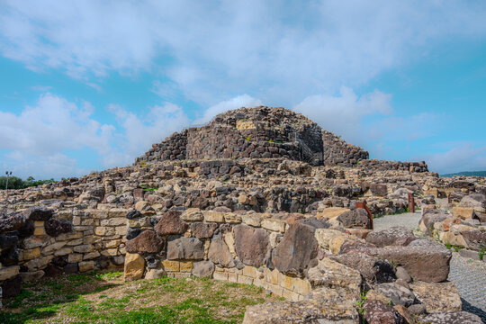 Nuraghe en pierres de basalte sur un paysage vert de Sardaigne sous un ciel bleu nuageux, vestige de la civilisation nuragique sarde