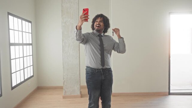 Man holding red smartphone and house key, hands visible, tapping phone and smiling inside a building; property success confidence.