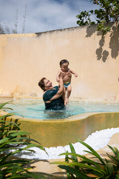 Joyful grandmother lifts her baby in a refreshing pool on a sunny day