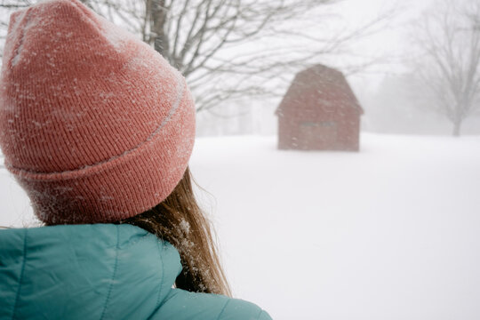 anonymous woman wearing snowy pink hat with red barn in snowstorm 