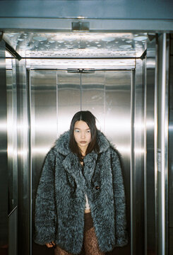 Young Person in a Coat Stands in an Elevator With Metal Walls