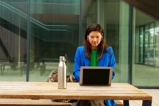 Woman Sits at Table Using Laptop With Water Bottle Nearby 