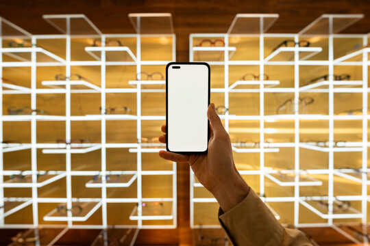 Hand holding smartphone with blank screen in optical shop