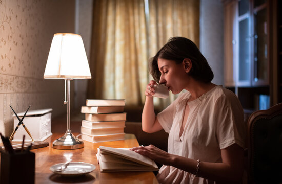 Young woman reading book and drinking hot beverage