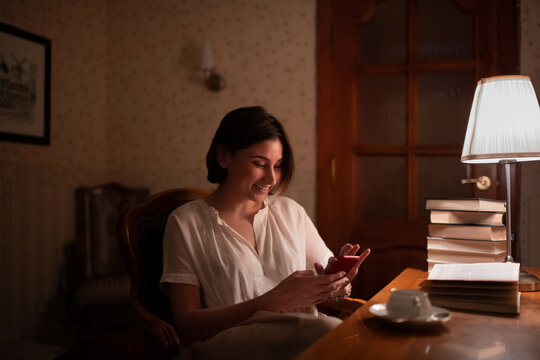 Cheerful female bookworm using smartphone near books