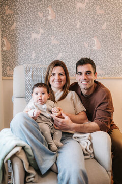 Parents holding baby in nursery chair smiling at home