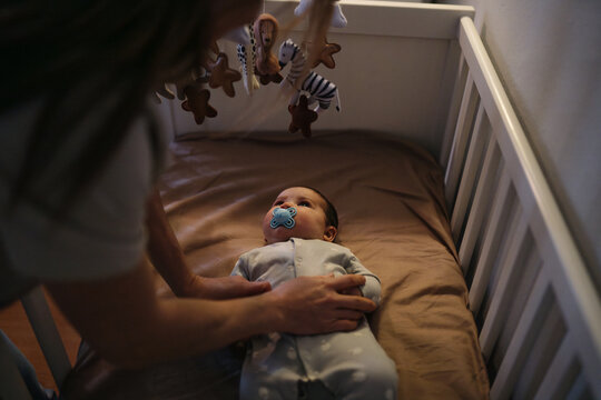 Parent comforting baby in crib with pacifier