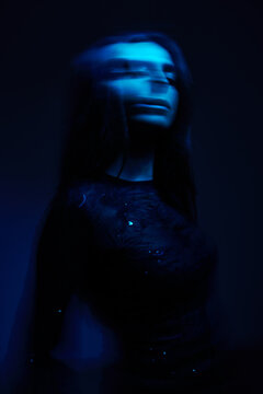 Woman in dark clothing stands in blue light and moves softly