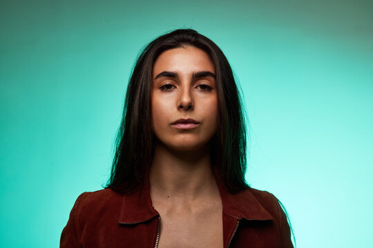 Woman standing against turquoise background with neutral express