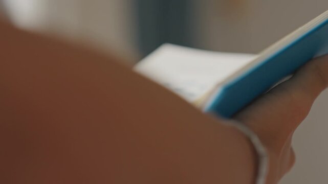 Holding hotel brochure steadily. Arm tightly holding booklet with hotel amenities and icons visible. Steady hand holding hotel brochure with silver bracelet and page icons clearly displayed