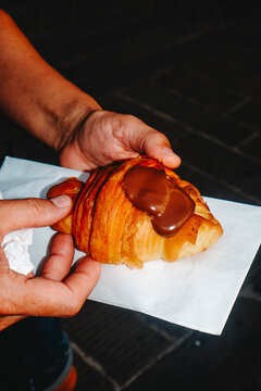 a man holding a chocolate filled croissant outdoors