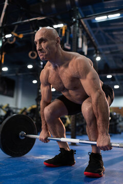 Bald elderly athlete squatting with barbell