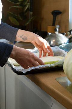 Woman preparing raw cabbage slices on baking sheet