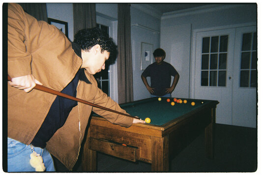 Men Playing Pool in a Room With a Green Table and Two Cues