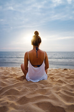 Woman doing yoga exercises and watching the sunset by the sea