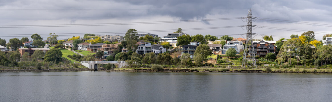 Panoramic view of the Maribyrnong River in Ascot Vale, Melbourne, featuring waterfront houses on a lush green riverbank with a high-voltage power line tower. Affluent and liveable suburban living 