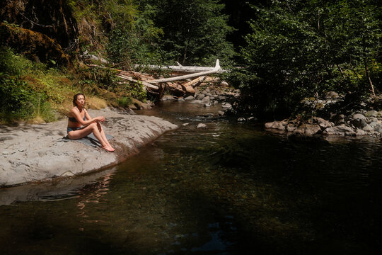 Woman Sitting by a Riverbank in a Wooded Area During Daylight