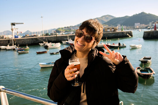 Woman enjoying beer making peace sign in harbor