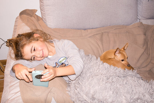 Child boy relaxing on sofa watching smartphone with dog